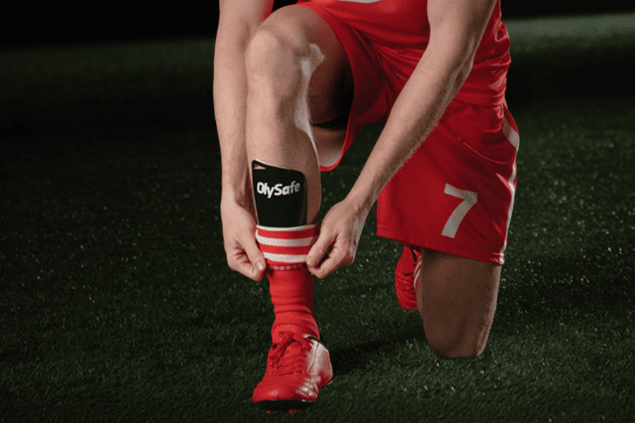 Football player in red OlySafe-branded kit tying boots on a grass pitch – OlyBet safe gaming space and responsible gambling features