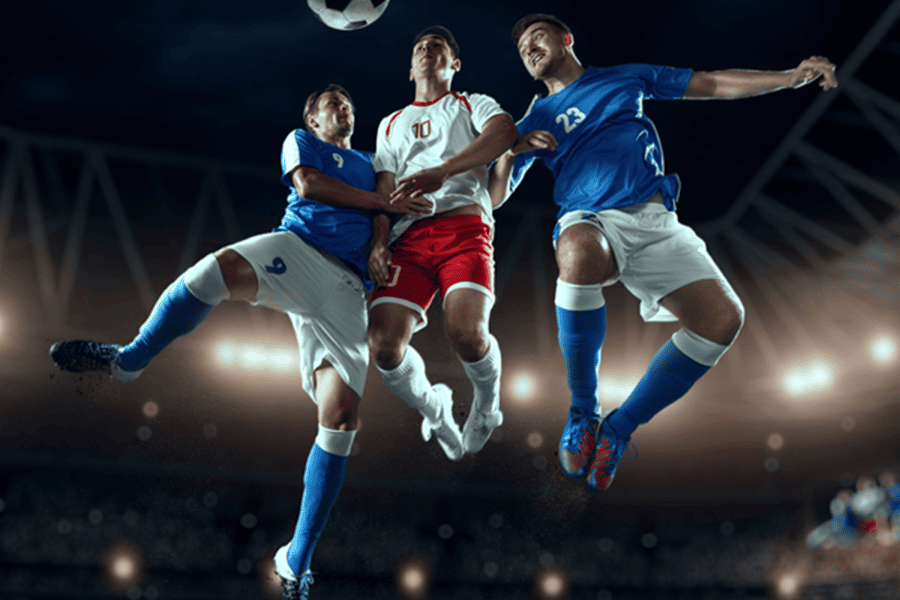 Three footballers competing for an aerial header under dramatic stadium floodlights – which football clubs have never been relegated from their national top flight